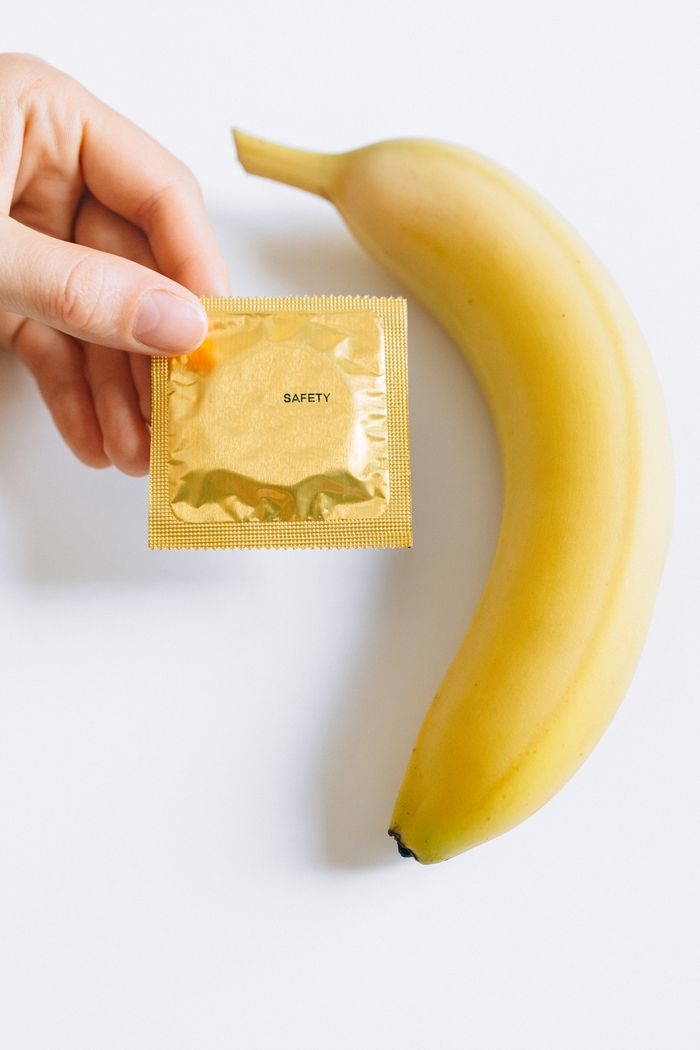 services-01 Close-up of a hand holding a condom package beside a banana highlighting safe sex education.