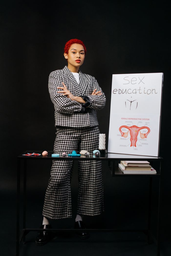 services-01 A confident woman with red hair stands by a table with sex education materials, emphasizing empowerment and education.